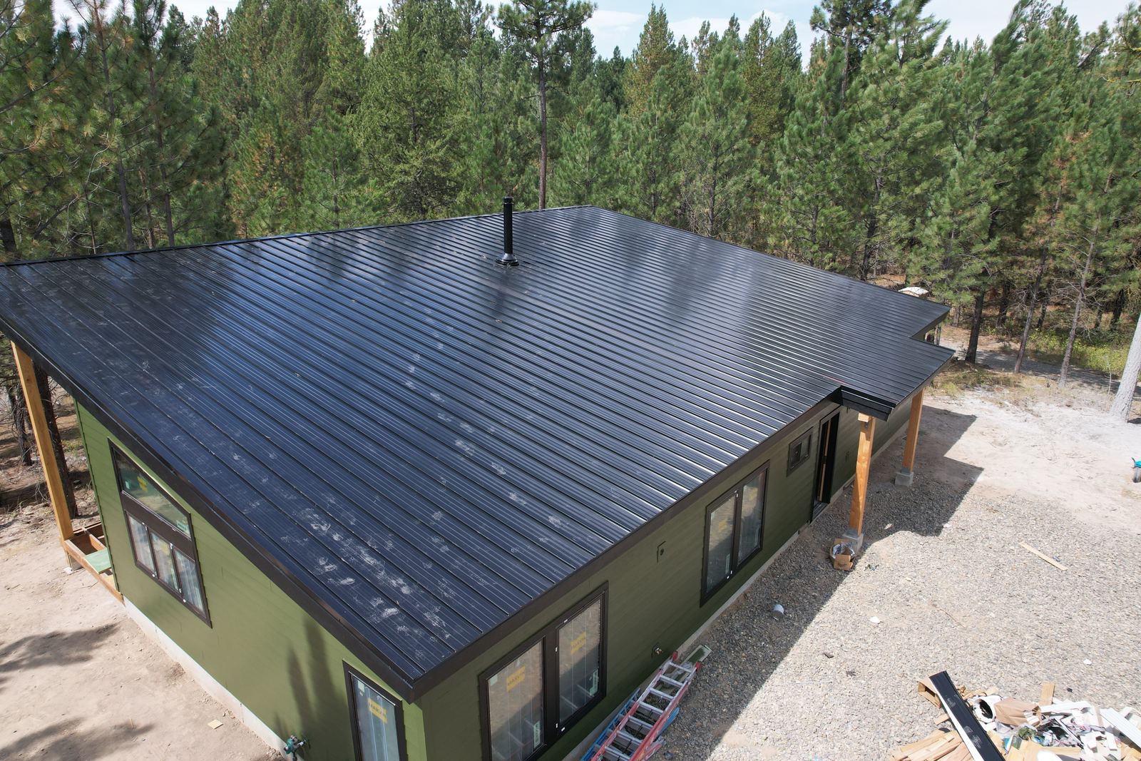 Black standing seam metal roof on a green sided house in the pines in Cascade, installed by Bork Roofing.