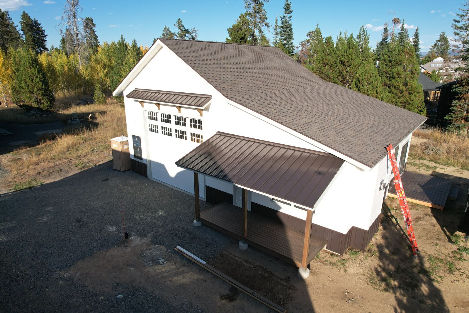 White house with a finished brown asphalt shingle roof and a brown metal porch roof in Donnelly, Idaho, installed by Bork Roofing.