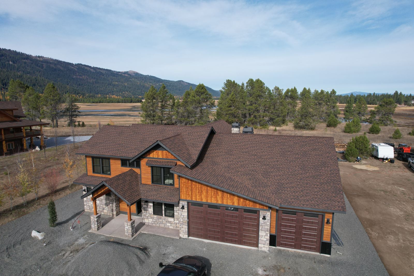 Aerial view of a brown asphalt shingle roof on a large home with a stone entry in Donnelly, Idaho, installed by Bork Roofing.