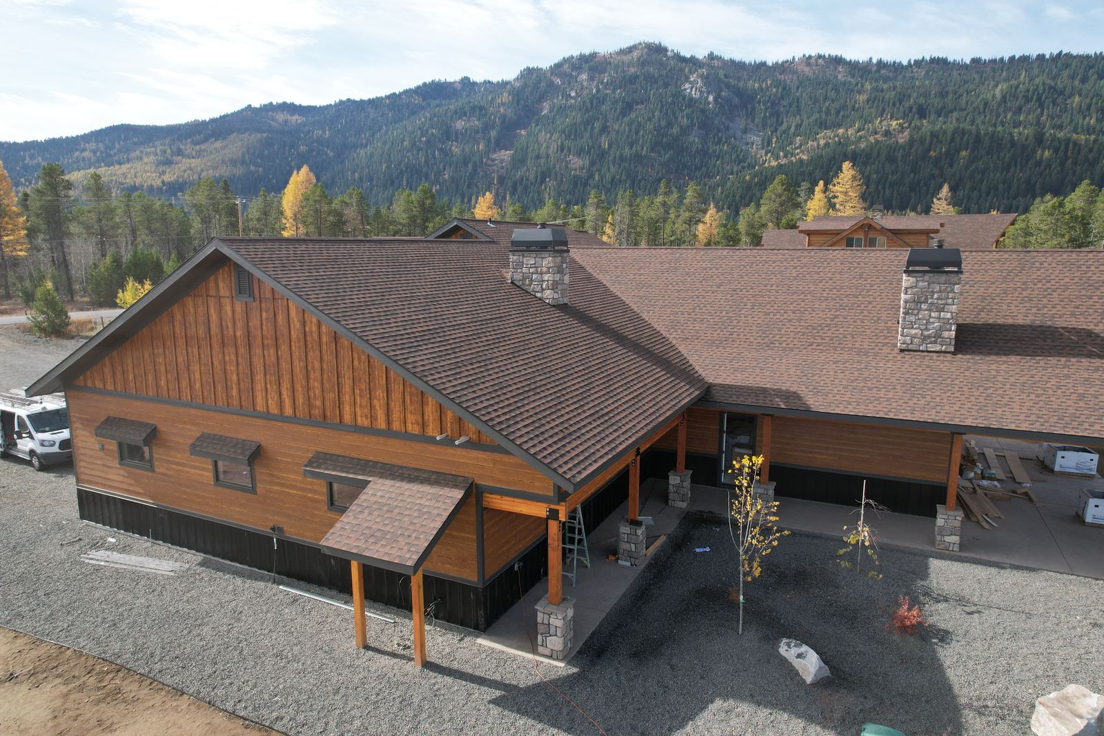 Brown asphalt shingle roof on a long wood sided building with two stone chimneys in Donnelly, Idaho, installed by Bork Roofing.