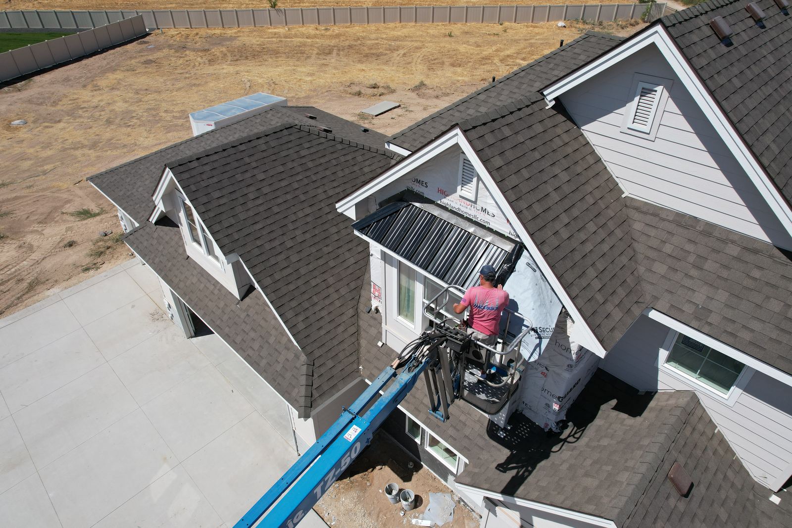 Drone view of a worker on a lift setting a black metal awning on a new home with a dark asphalt shingle roof in Eagle.