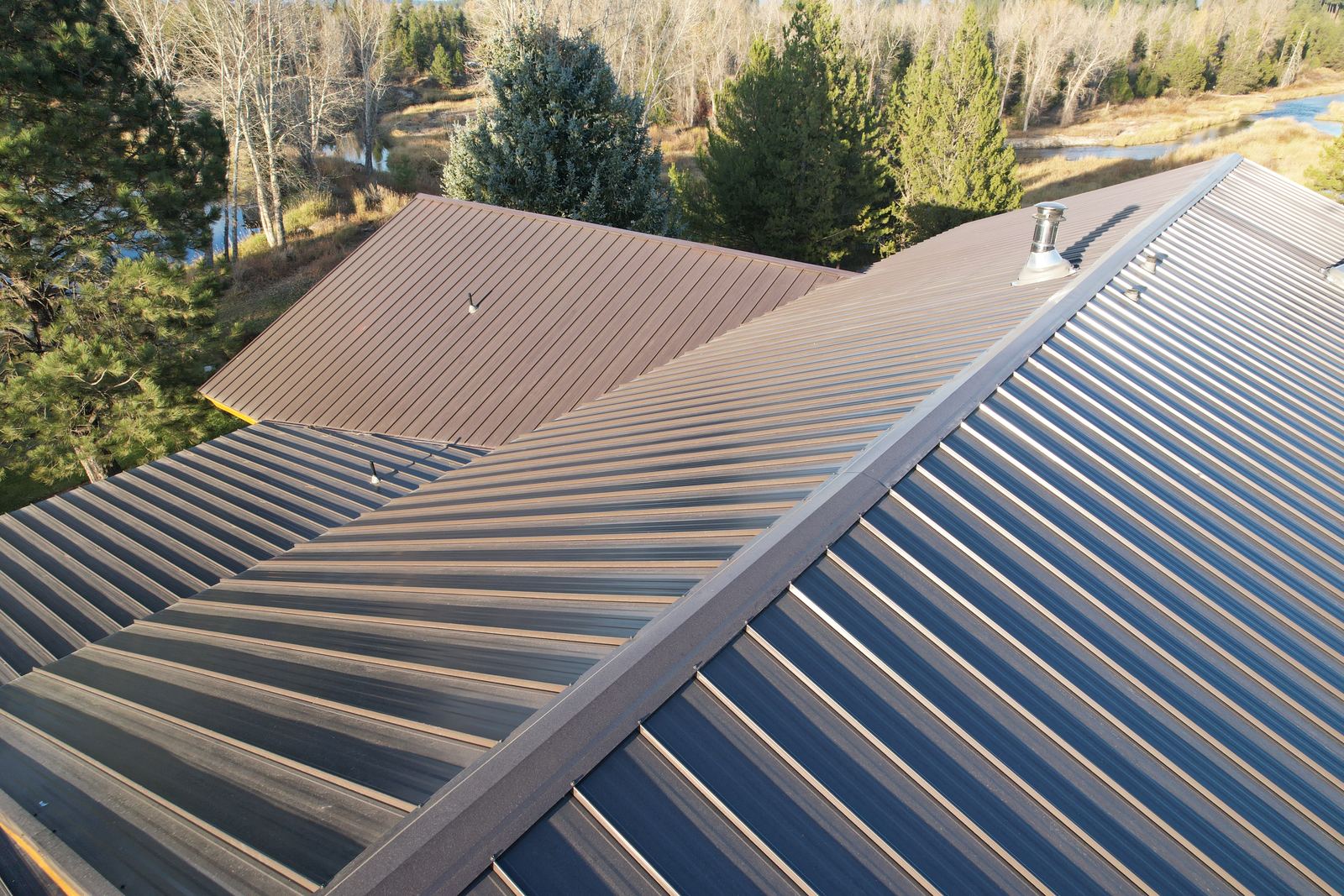 Brown standing seam metal roof on a McCall home with a river and pines behind it, installed by Bork Roofing.