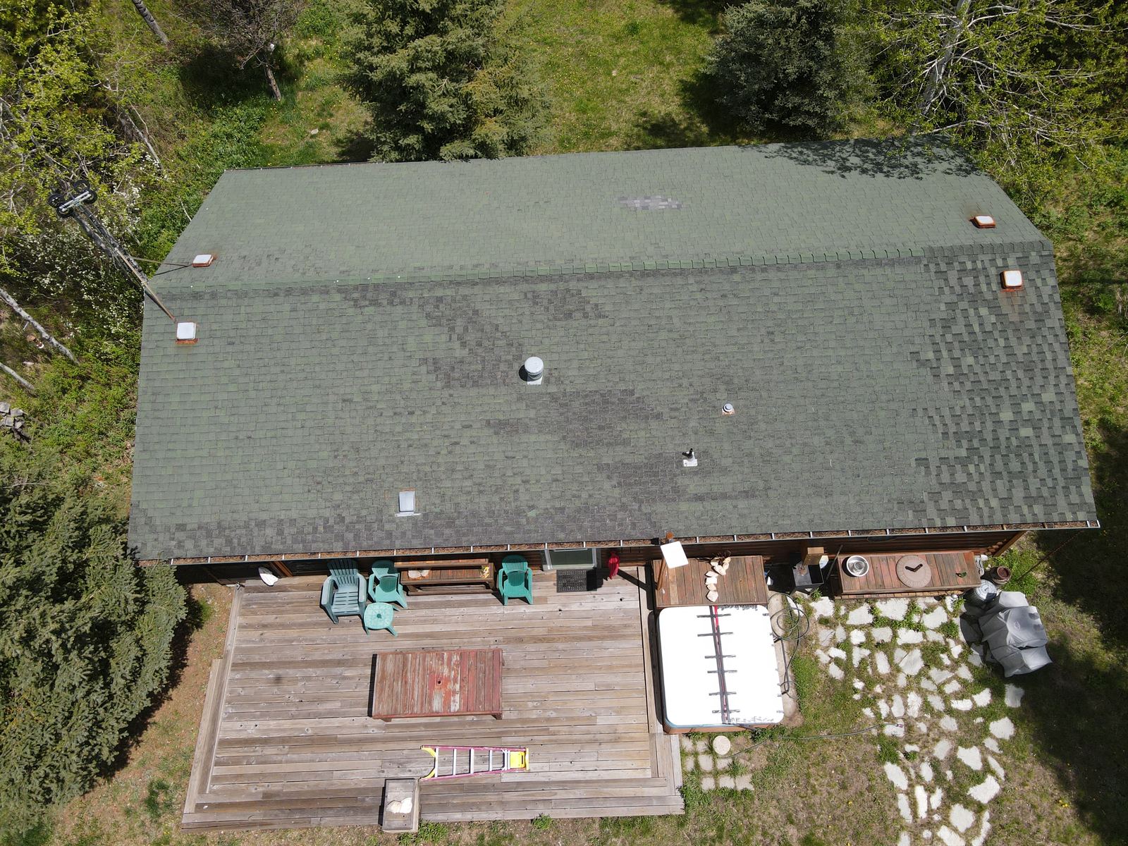 Aerial view of a worn green asphalt shingle roof on a Donnelly cabin with a wood deck below.