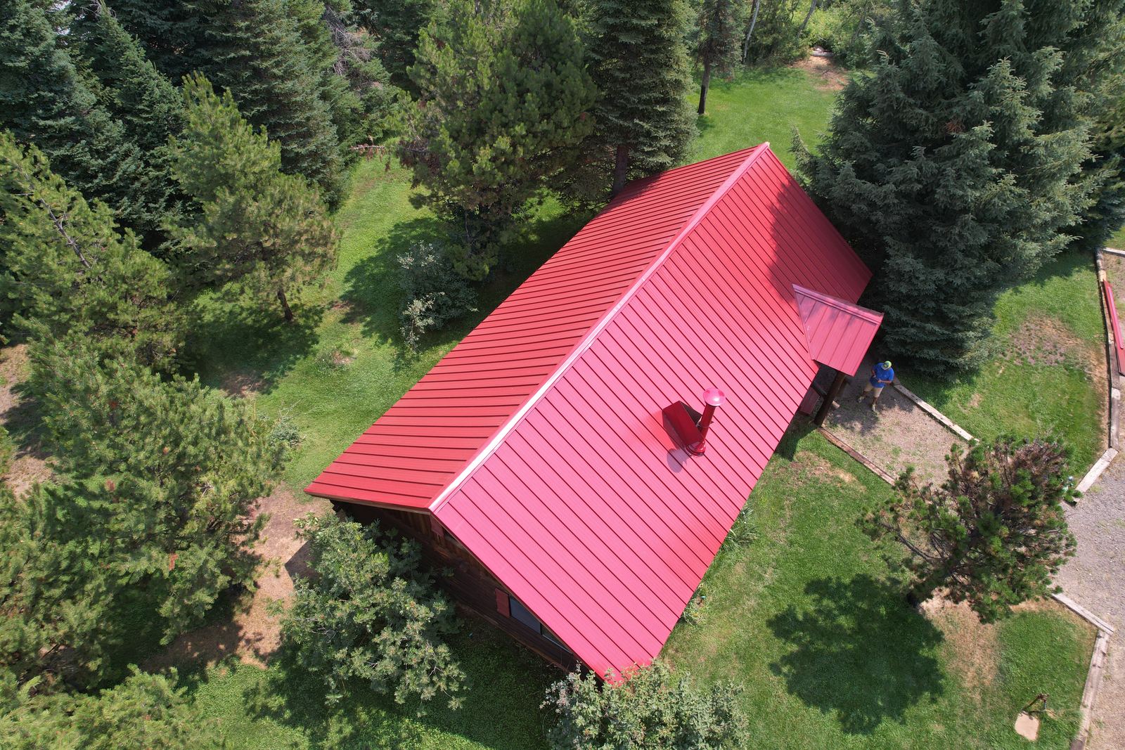 Aerial view of a red standing seam metal roof on a Donnelly cabin surrounded by pine trees, installed by Bork Roofing.