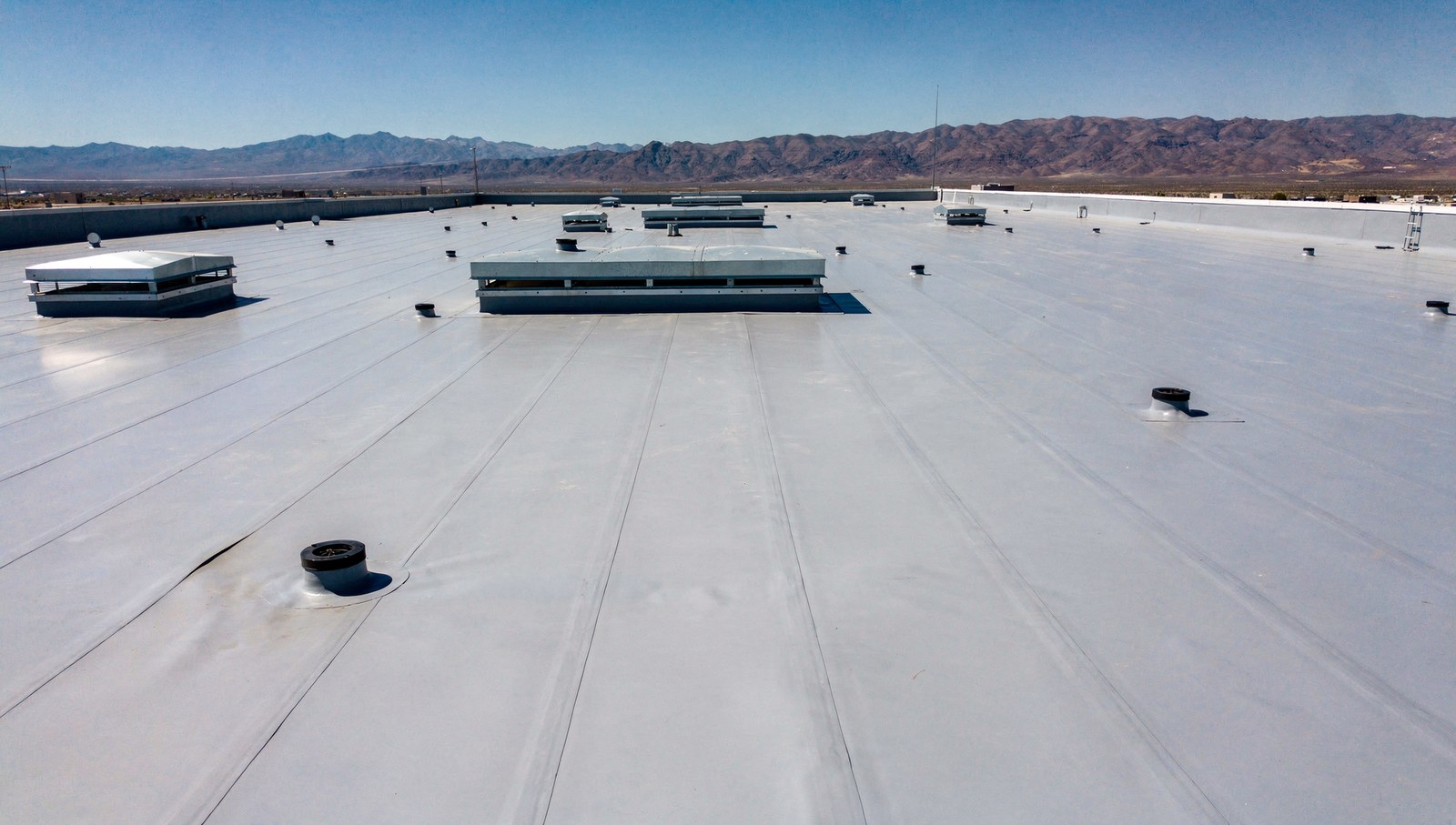 Flat low slope roof covered in light grey membrane with mechanical curbs and drains