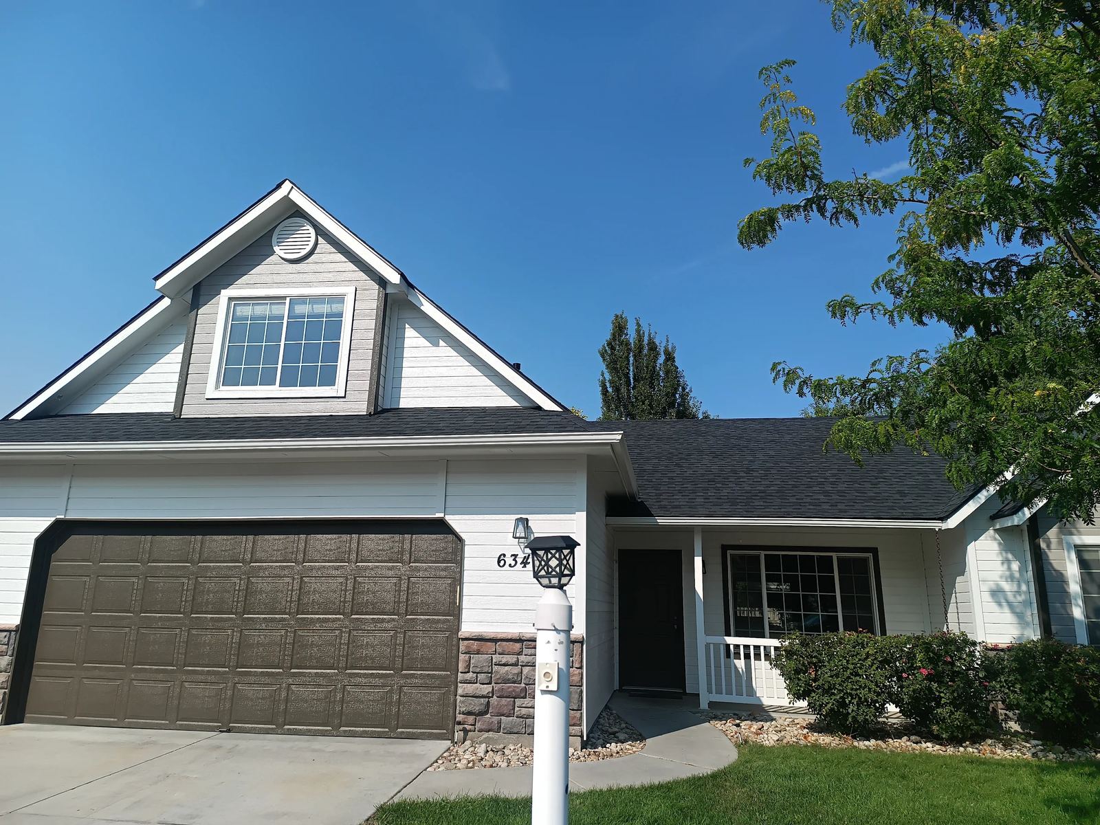 Front of a two story house with white siding, a brown garage door and a new dark asphalt shingle roof in Nampa, installed by Bork Roofing.