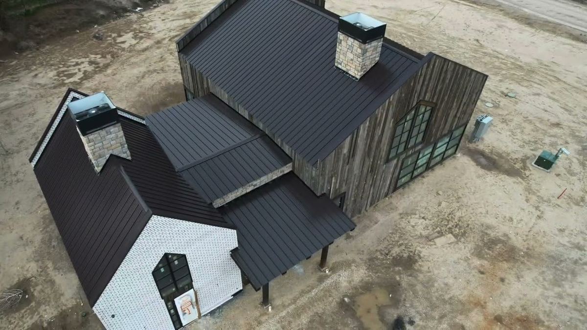Dark brown standing seam metal roof on a new build with reclaimed wood siding and stone chimneys